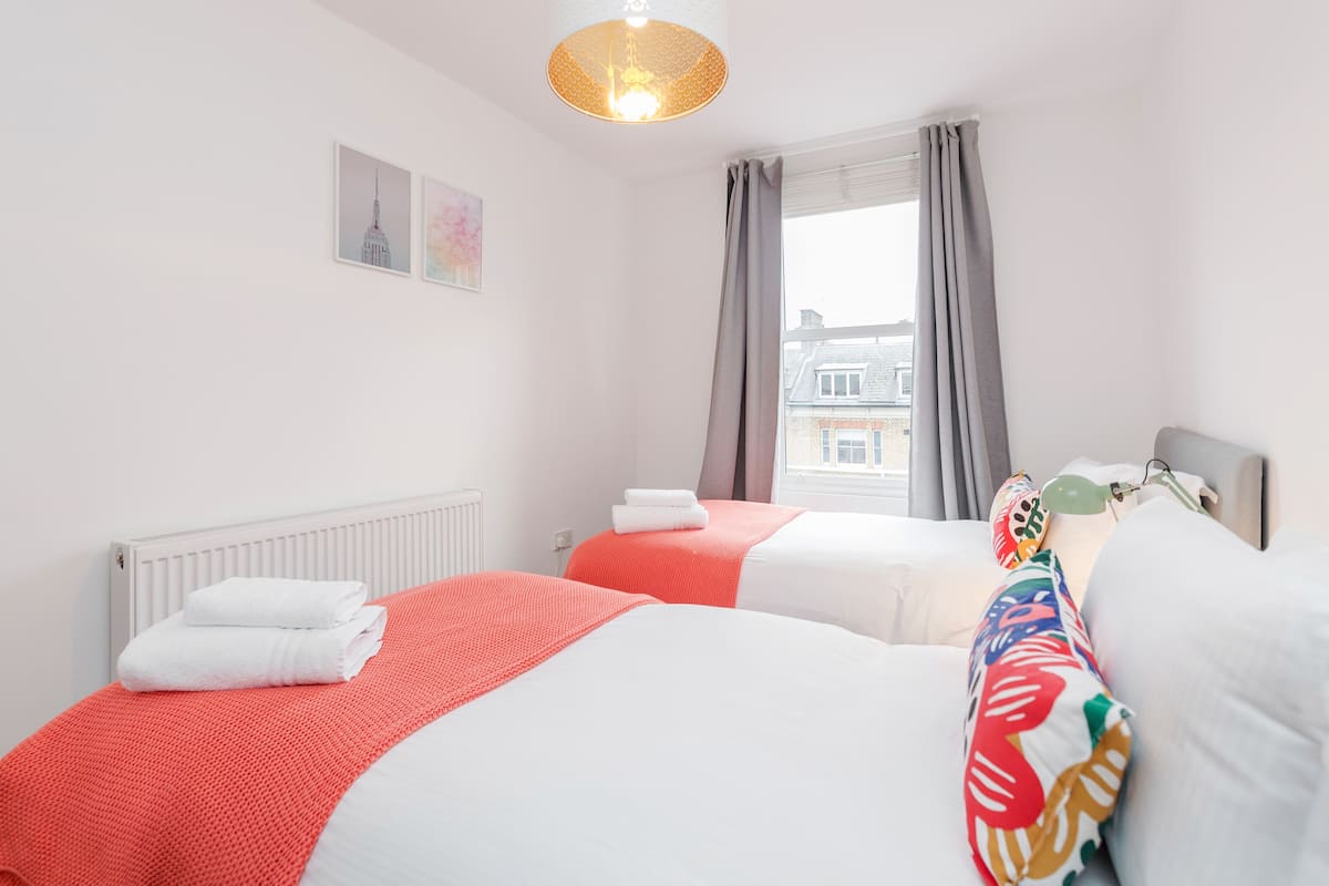 Een hotelkamer met twee bedden, een radiator, een raam met gordijnen en een hanglamp.