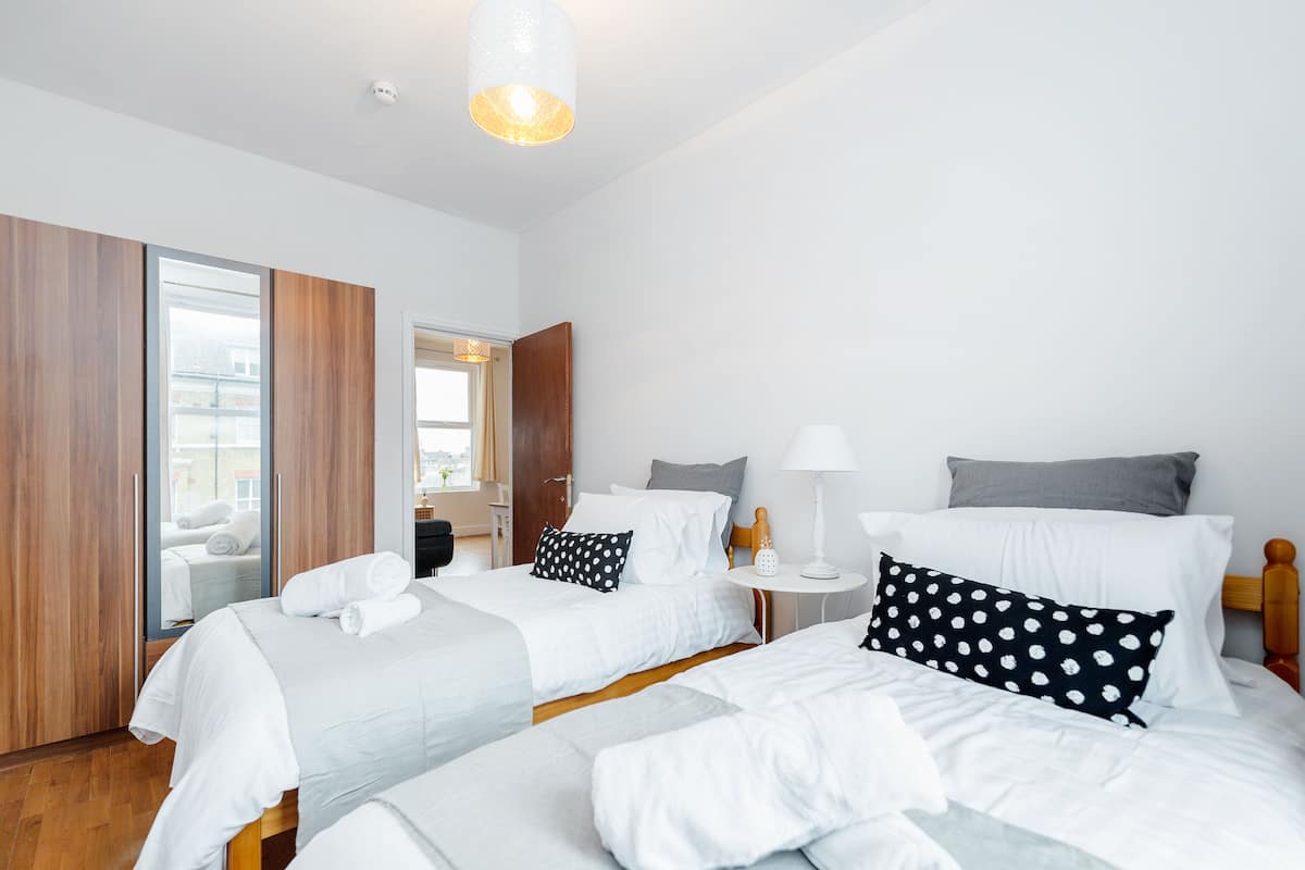 Een hotelkamer met twee bedden, een houten garderobe, een klein nachtkastje met een lamp en een grote spiegel.
