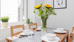 A dining table set with white plates, bowls, and glasses, a vase with yellow flowers, and a framed picture on the wall. - WelcomeStay Clapham Junction 2 bedroom Apartment (London)