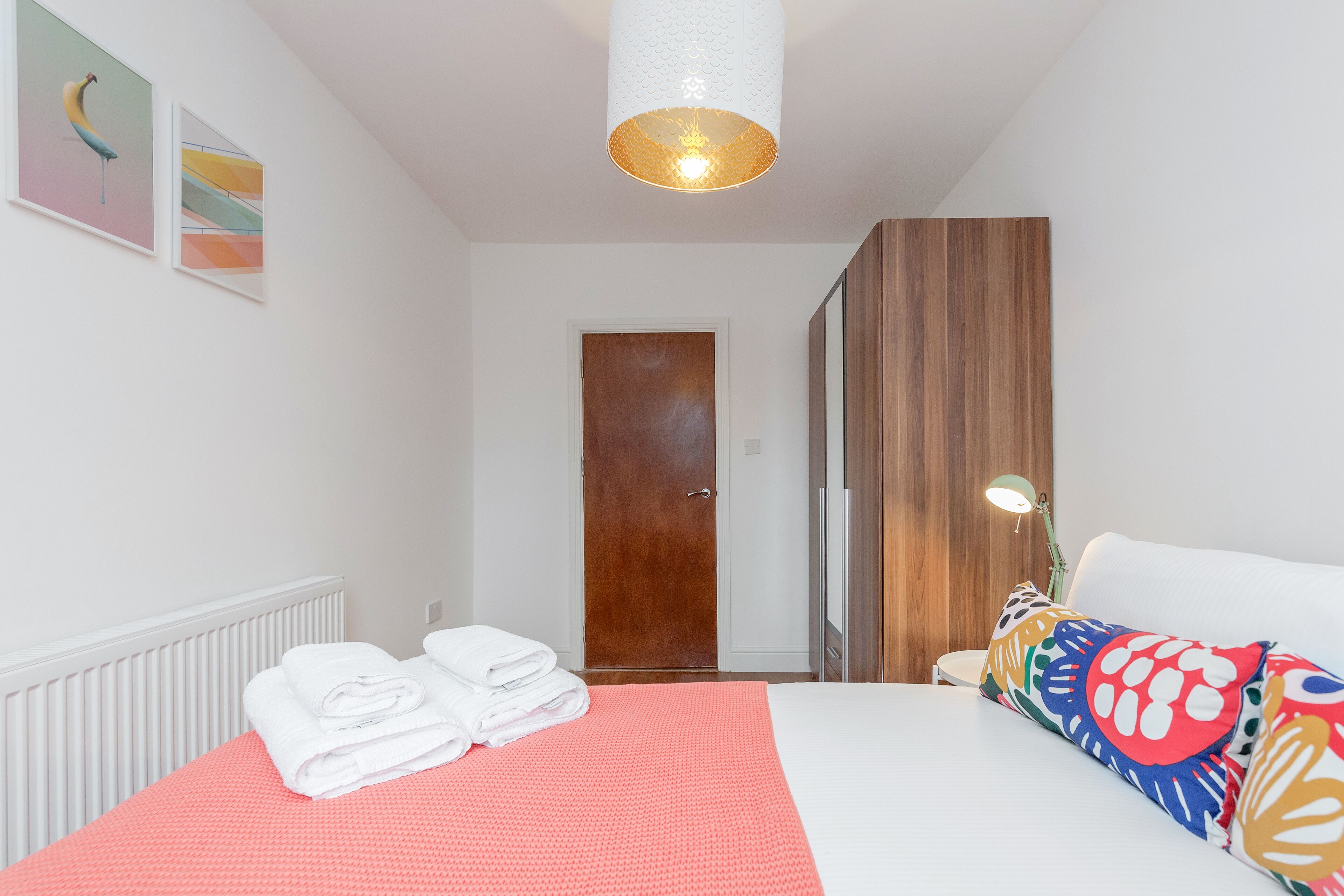 Une chambre d’hôtel avec un lit, une armoire en bois, une porte et un luminaire fixé au mur.