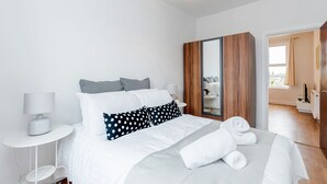 A modern hotel room with a neatly made bed, a wooden wardrobe, and a bathroom visible through an open door. - WelcomeStay Clapham Junction 2 bedroom Apartment (London)
