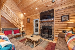 A log cabin interior with a staircase, a fireplace, a sofa, and a television.