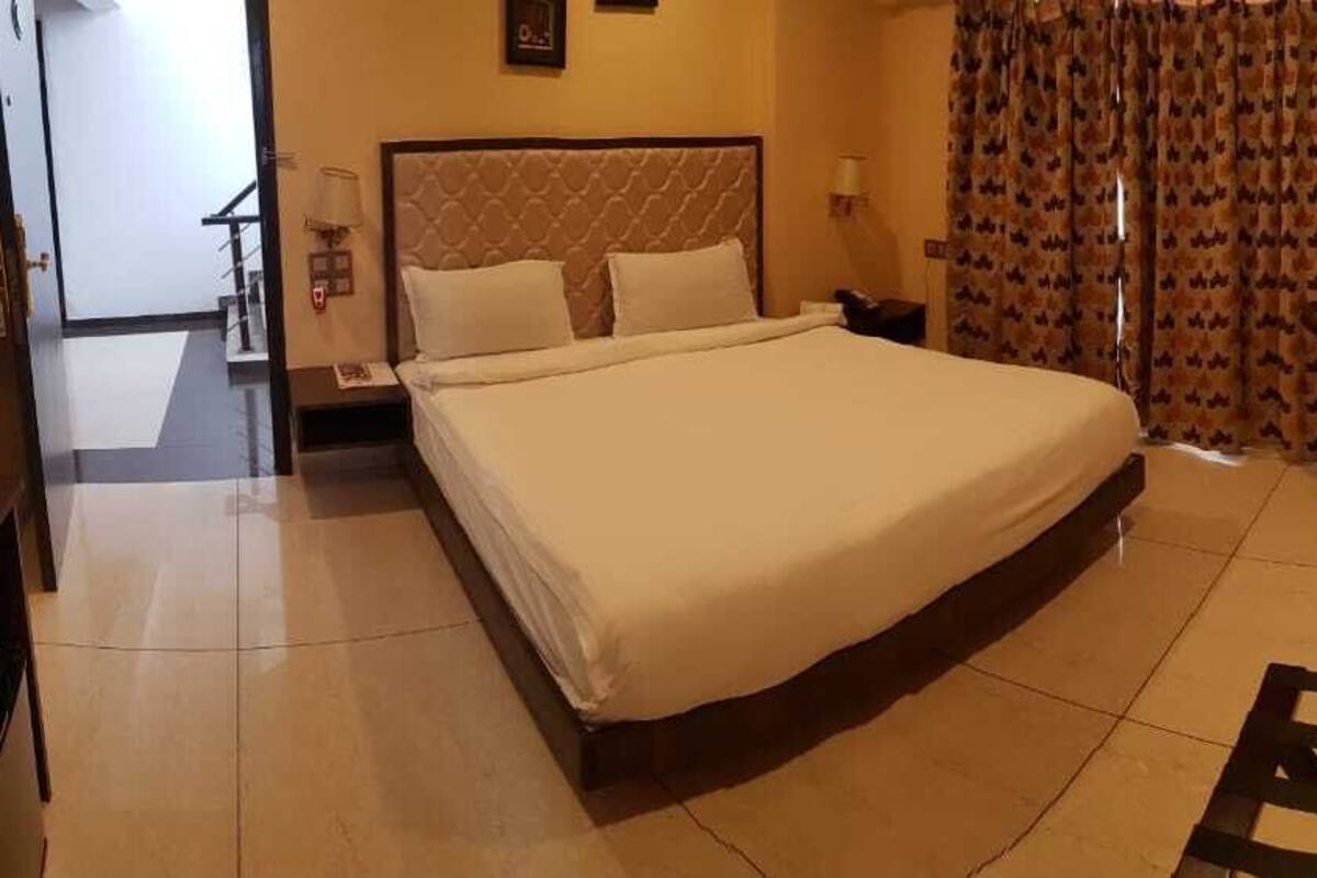 A hotel room with a large bed, a desk, a chair, and a view of the hallway.