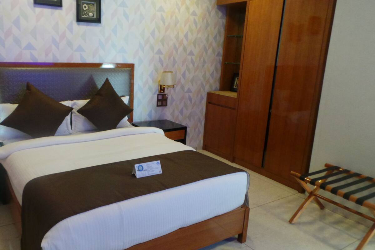A neatly made bed with a headboard, two bedside tables with lamps, a wooden wardrobe, and a small wooden chair.