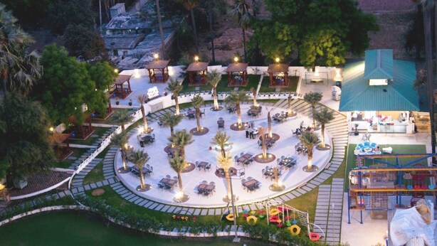 Vista aérea de um resort com área de estar circular ao ar livre, cercada por palmeiras e uma piscina.