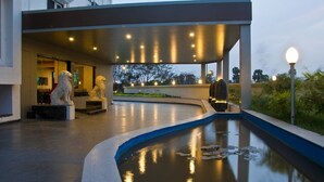 Um edifício moderno com área externa coberta, apresentando piscina com folhas de nénufr e duas estátuas de leão.