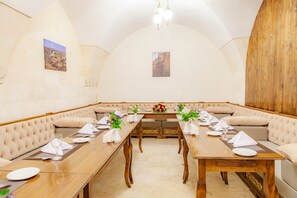 A dining area with a long wooden table set for a meal, cushioned seating, and artwork on the walls.