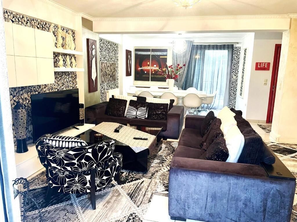 A living room with a sofa set, a television, and a dining area with a table and chairs.