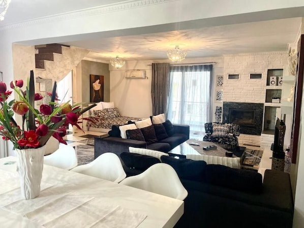 Uma sala de estar moderna com um conjunto de sofá, uma mesa de jantar com um vaso de flores e uma lareira.