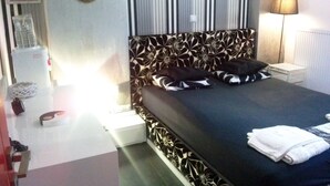 Et soveværelse med en seng, puder, et natbord, en lampe og en væg med en krans og indrammet tekst.