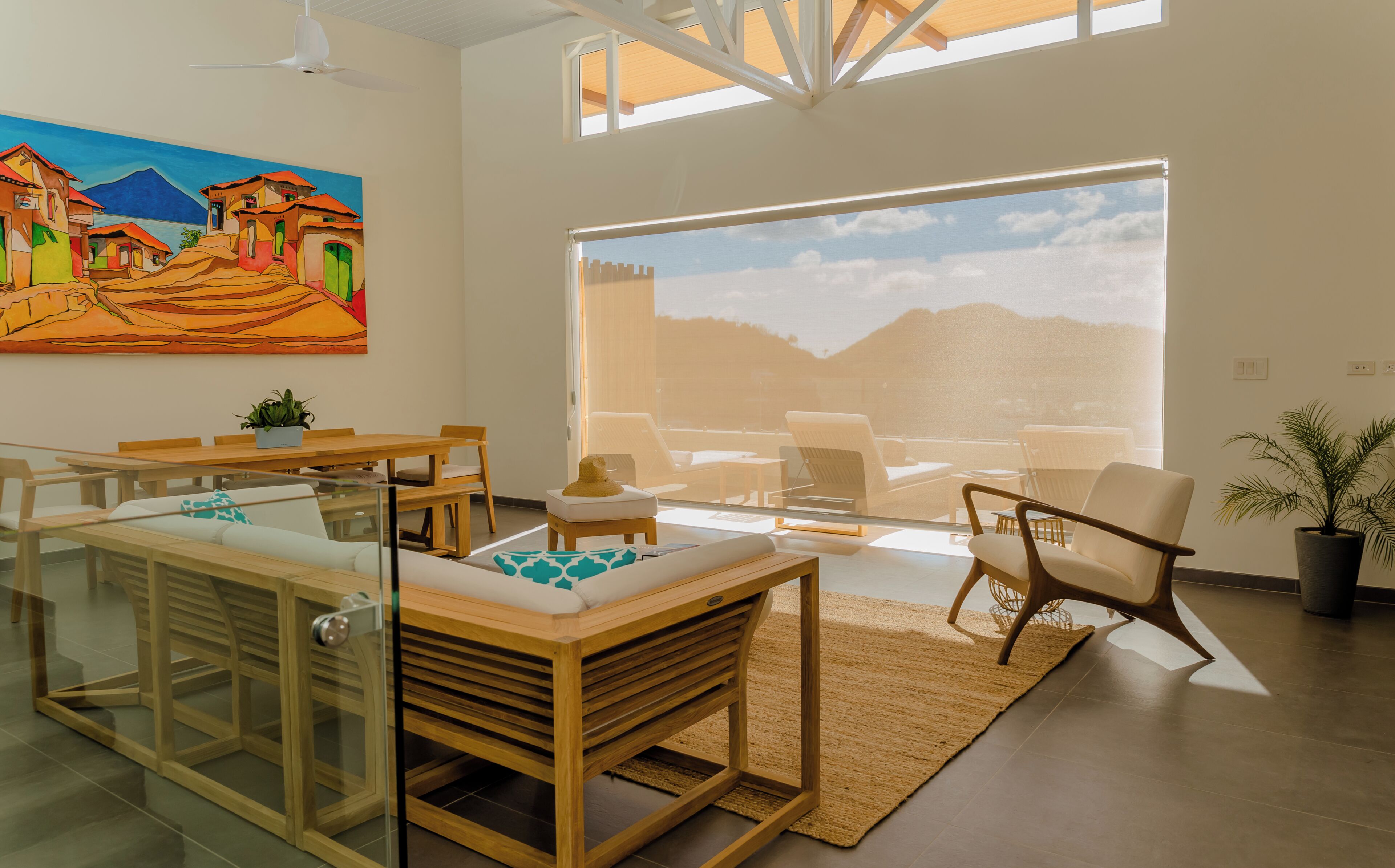 A modern living room with a large window, a dining area, and a painting of a village.