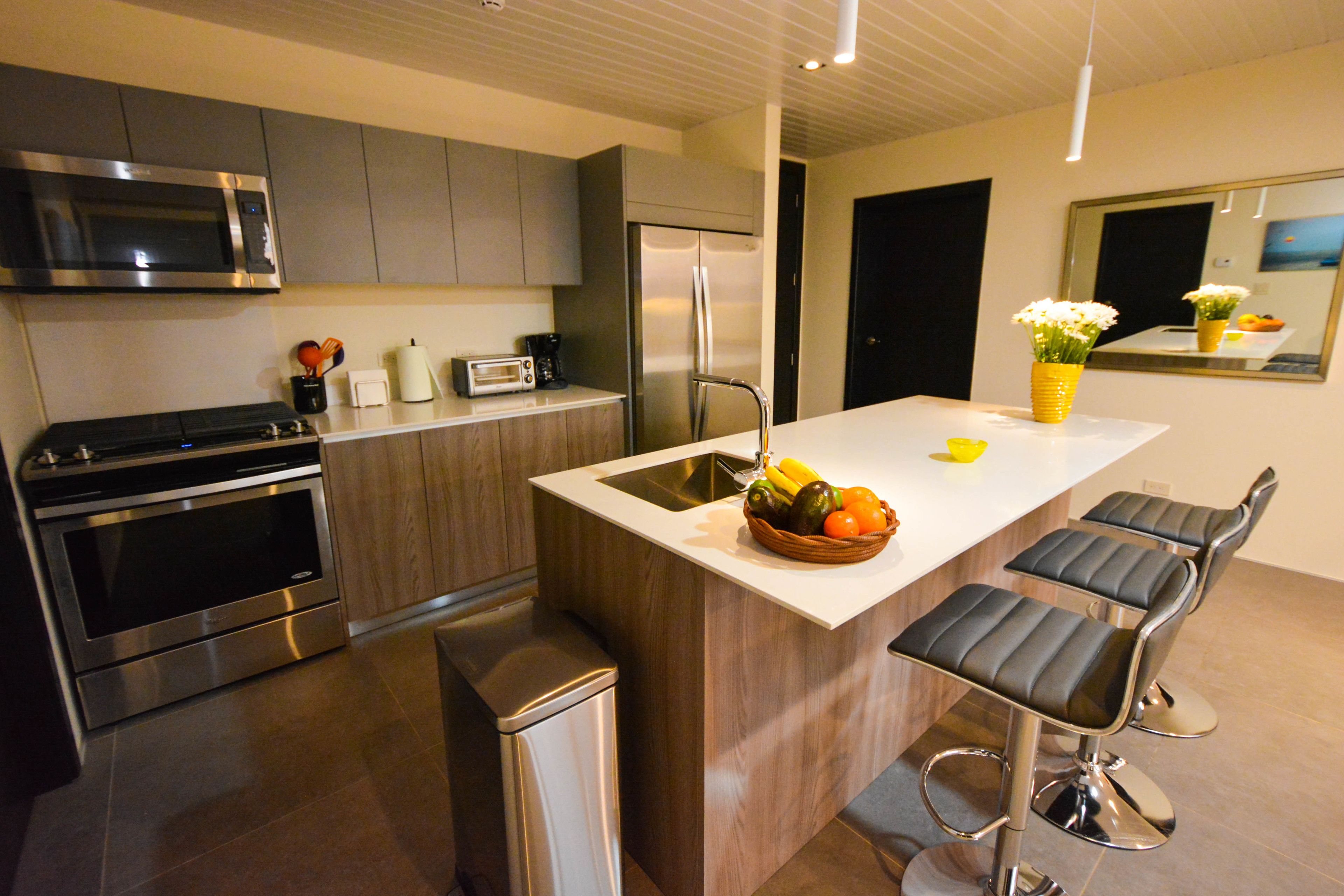 A modern kitchen with stainless steel appliances, a central island with bar stools, and a fruit bowl.