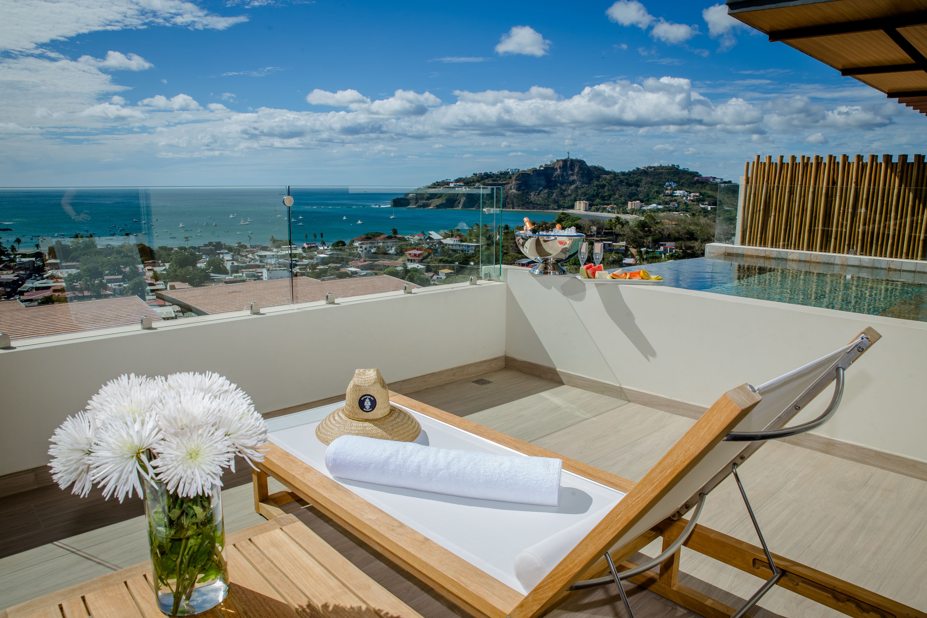 A balcony with a view of the sea, a lounge chair, a towel, and a vase with flowers. - La Santa Maria Boutique Hotel & Residences San Juan del Sur Nicaragua (San Juan del Sur)