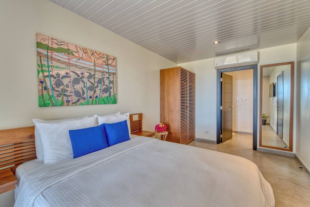 Een moderne slaapkamer met een groot bed, een houten hoofdbord, een kunstwerk aan de muur en een schuifdeur naar een andere kamer.