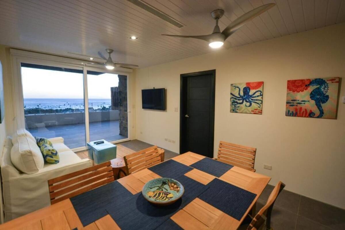 Een eethoek met een grote tafel, stoelen en uitzicht op de oceaan door grote ramen.