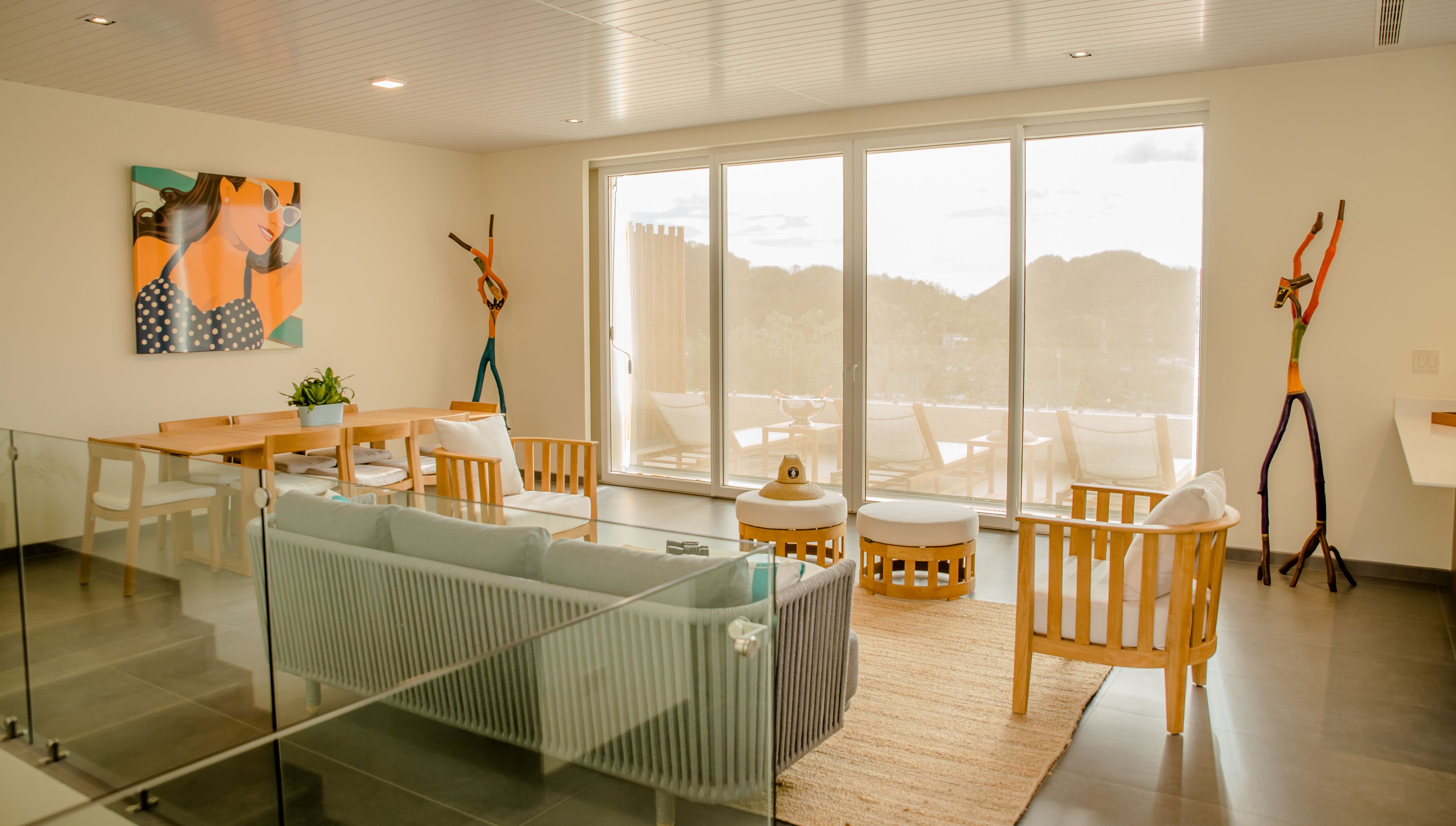 Een moderne hotelkamer met een glazen scheiding, een zithoek met een tafel en stoelen, een groot raam met uitzicht en een uniek sculptuur.