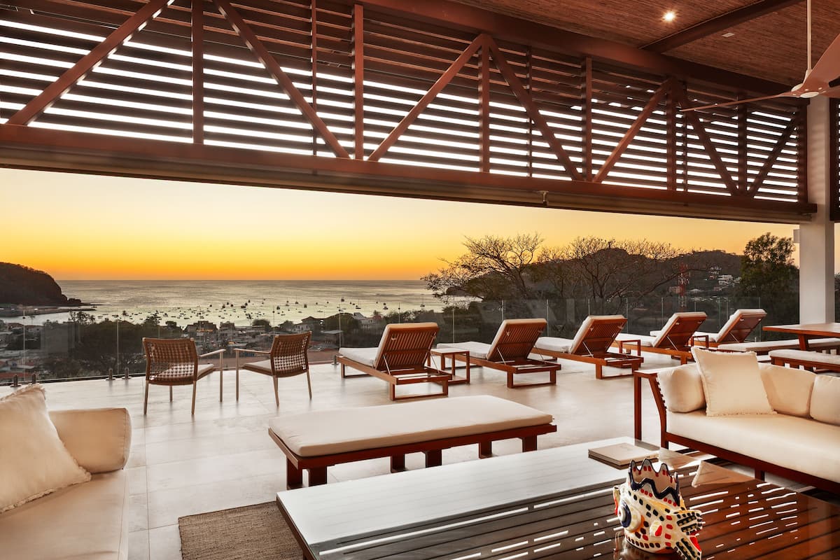 A sunlit outdoor lounge area with seating and a view of the ocean.