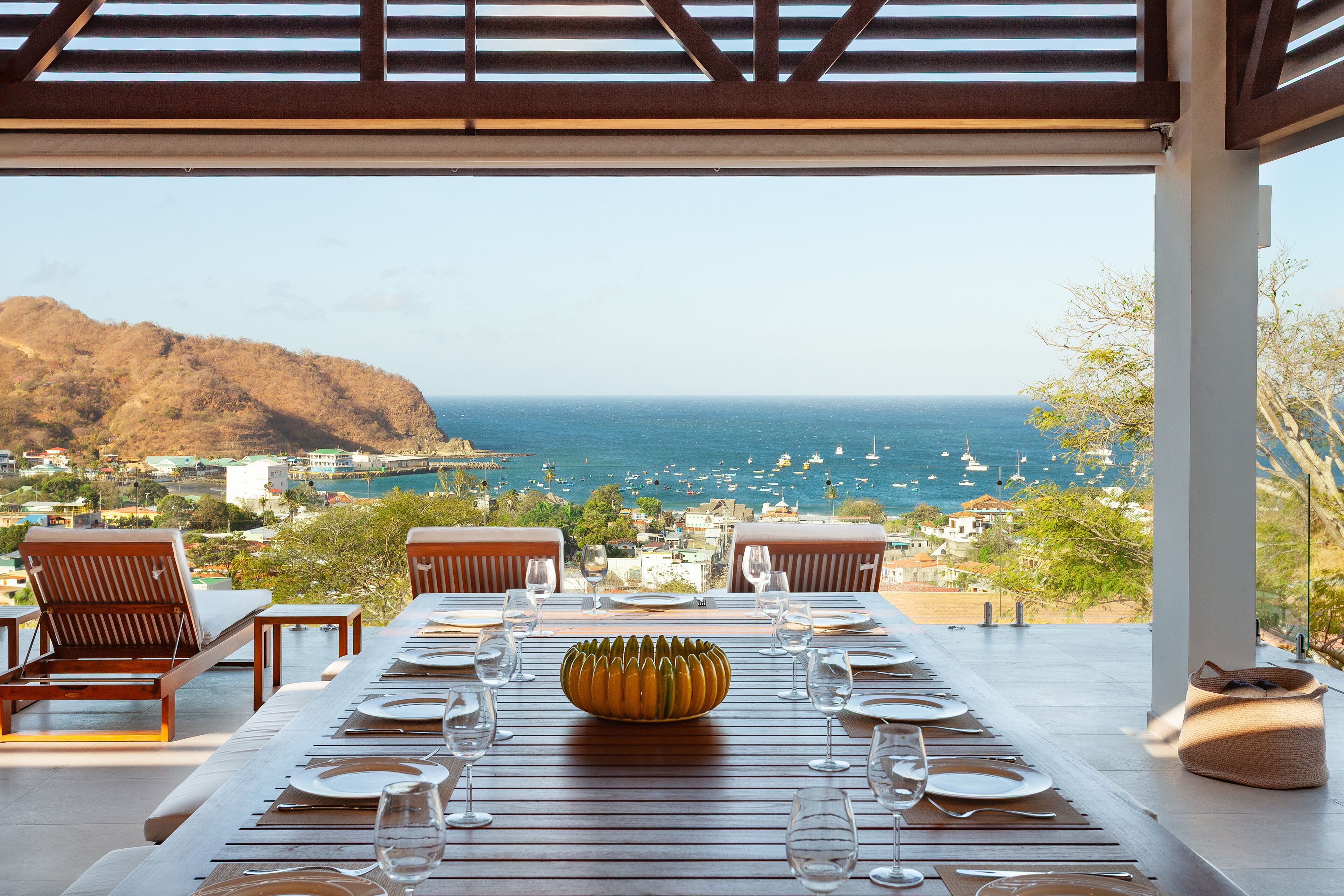 A dining table set for six with a view of the ocean and hills.
