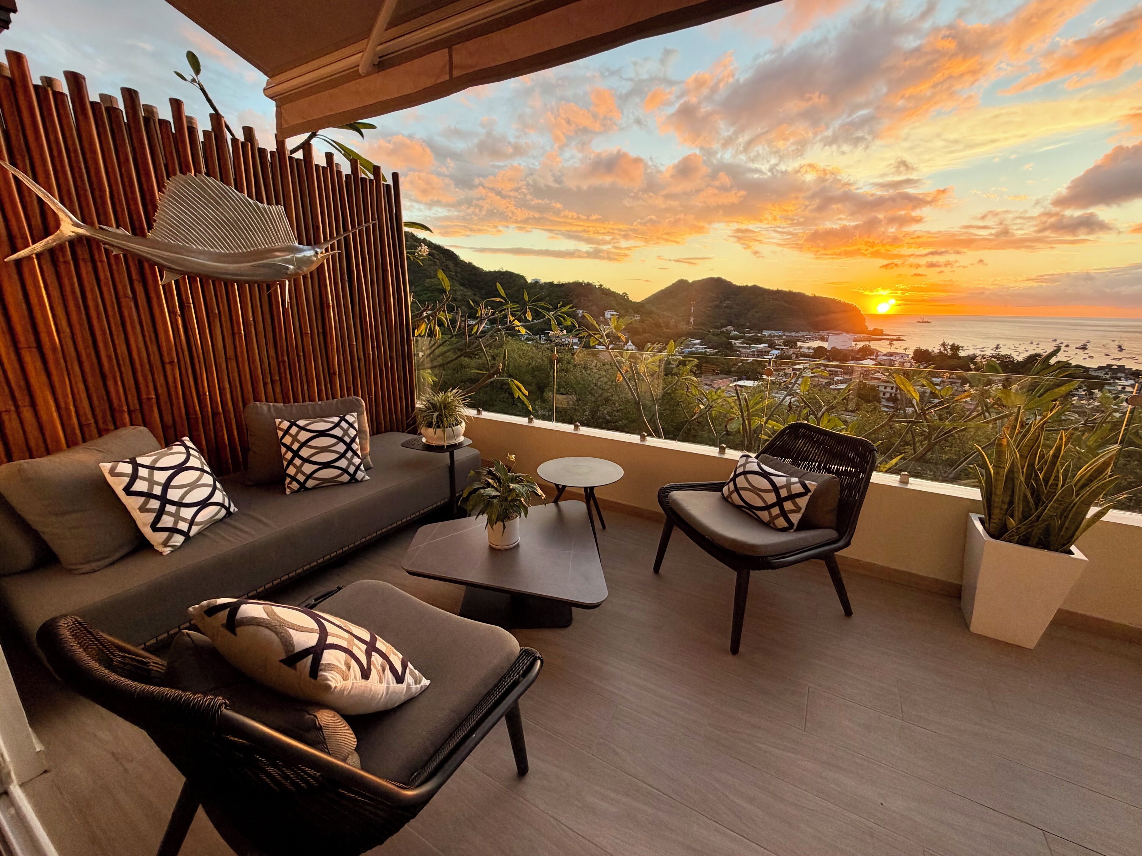 Un balcon agrémenté d’un canapé, de chaises et d’une table, offrant une vue imprenable sur un magnifique coucher de soleil.