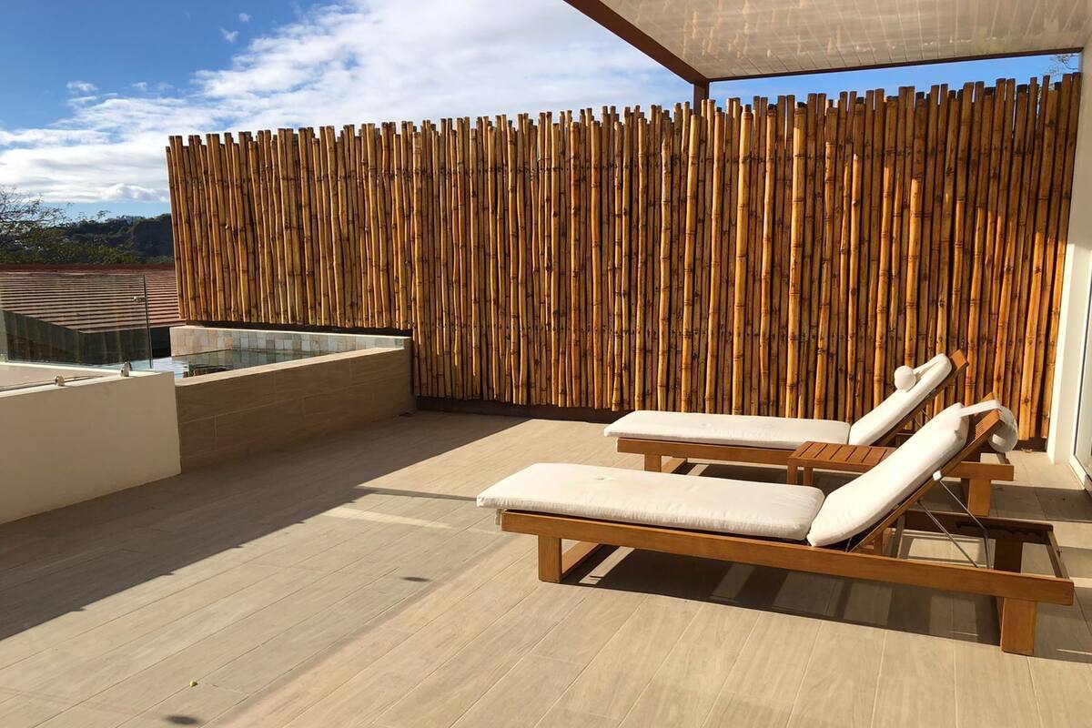 Een dakterras met twee houten ligstoelen en een bamboe muur.