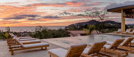 A poolside area with lounge chairs and a view of the ocean at sunset.