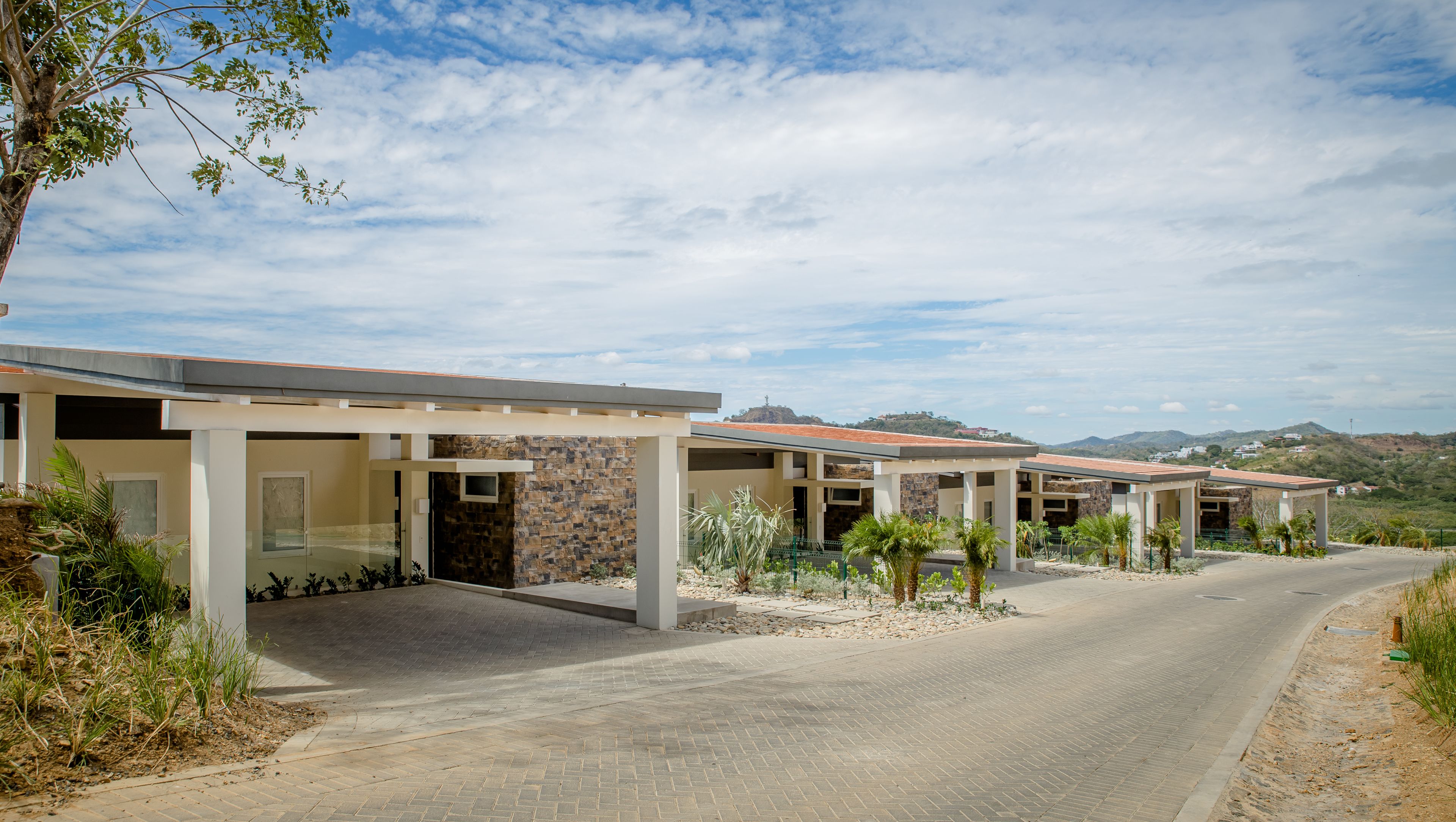 A modern building with multiple covered patios, stone walls, and a paved driveway.