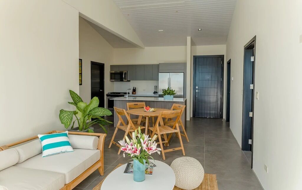 A modern living room with a sofa, a dining table with chairs, and a kitchen in the background.