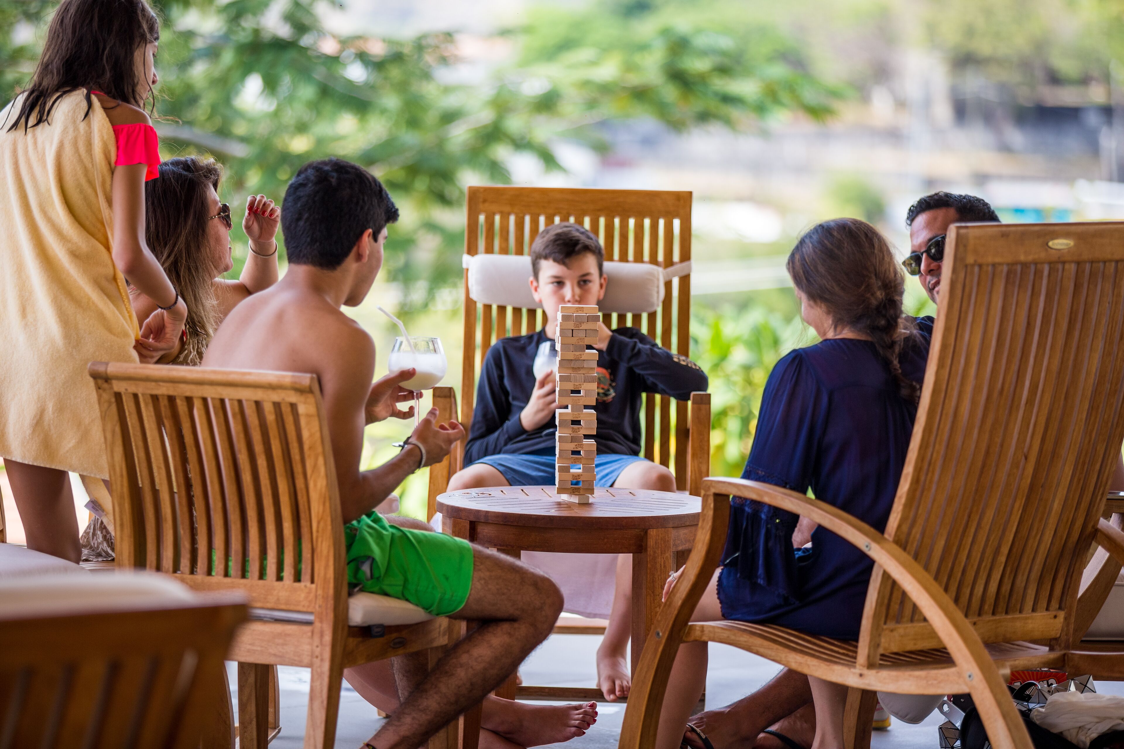 A group of people playing Jenga around a small wooden table outdoors.