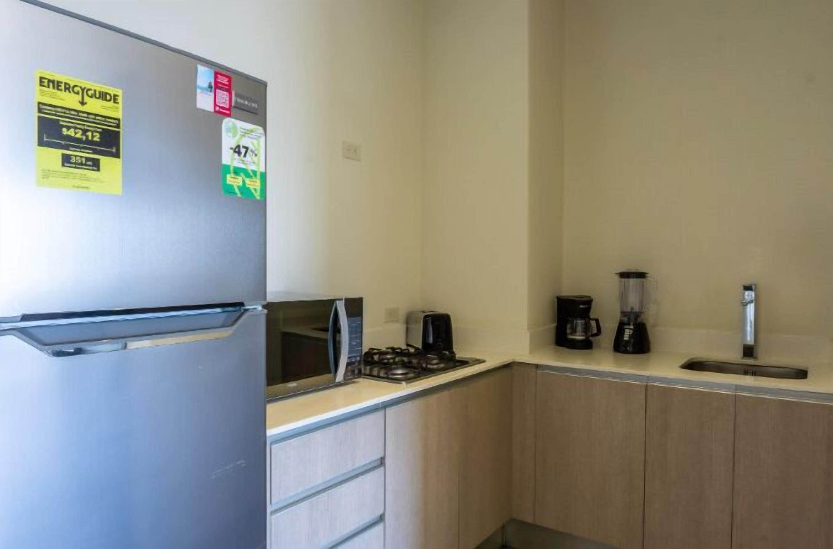 A compact kitchen with a refrigerator, microwave, stove, coffee maker, and blender.