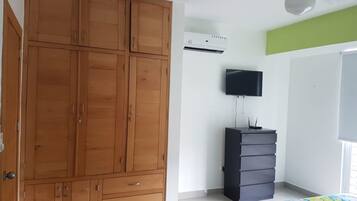A bedroom with a wooden wardrobe, a television, a dresser, and a ceiling fan.