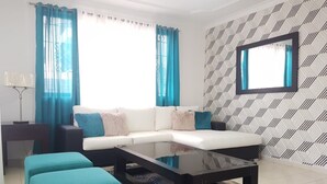 A modern living room with a white sectional sofa, teal armchairs, a glass coffee table, and patterned wallpaper. - Amarilis Masajes (Santiago de los Caballeros)