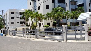 A multi-story building with a gated entrance, surrounded by palm trees and a clear sky. - Amarilis Masajes (Santiago de los Caballeros)
