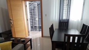 A dining area with a wooden table and chairs, a sofa, and a small table with decorative items. - Amarilis Masajes (Santiago de los Caballeros)