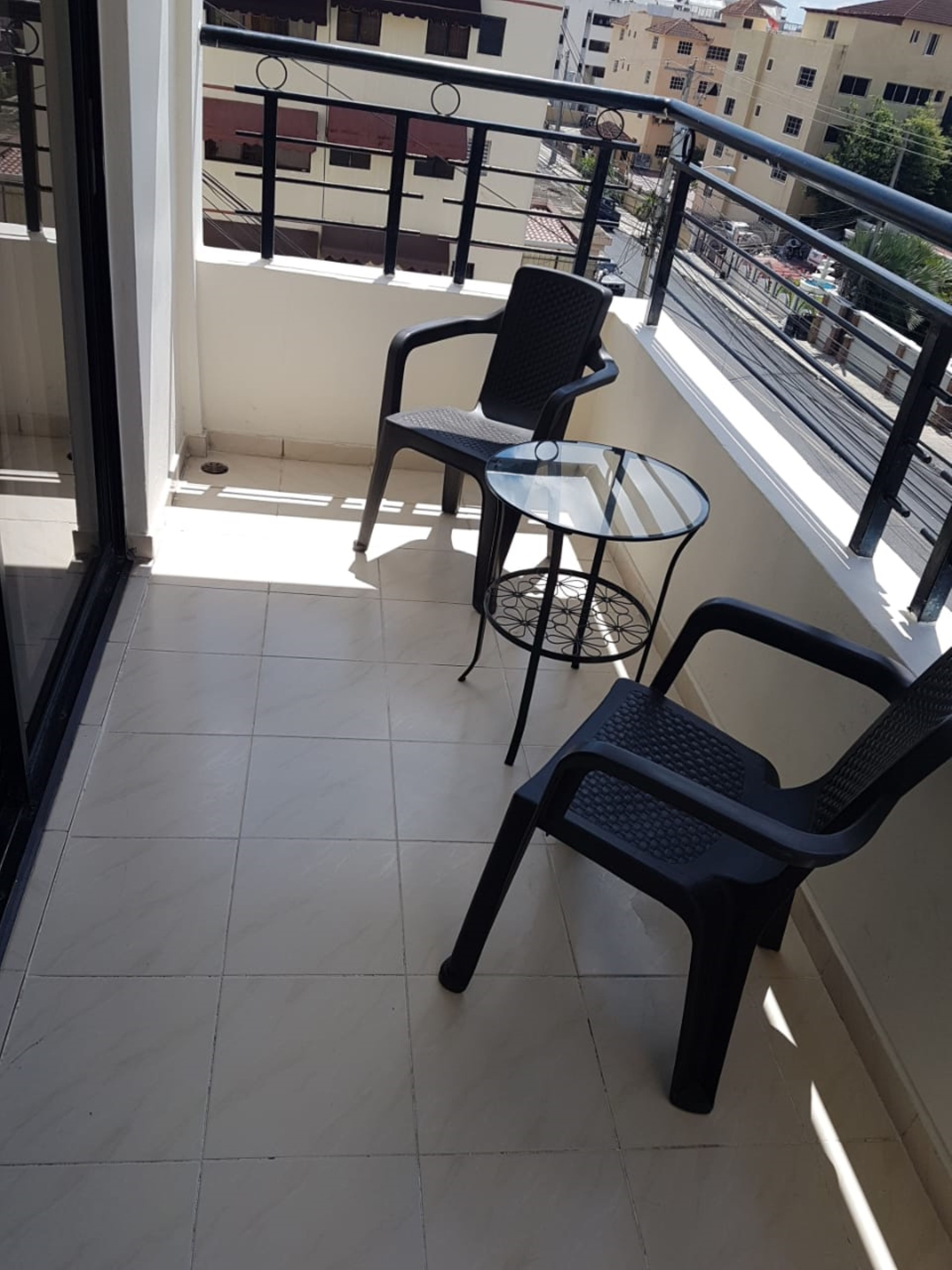 A balcony with two chairs and a small table, tiled floor, and a view of buildings in the background.