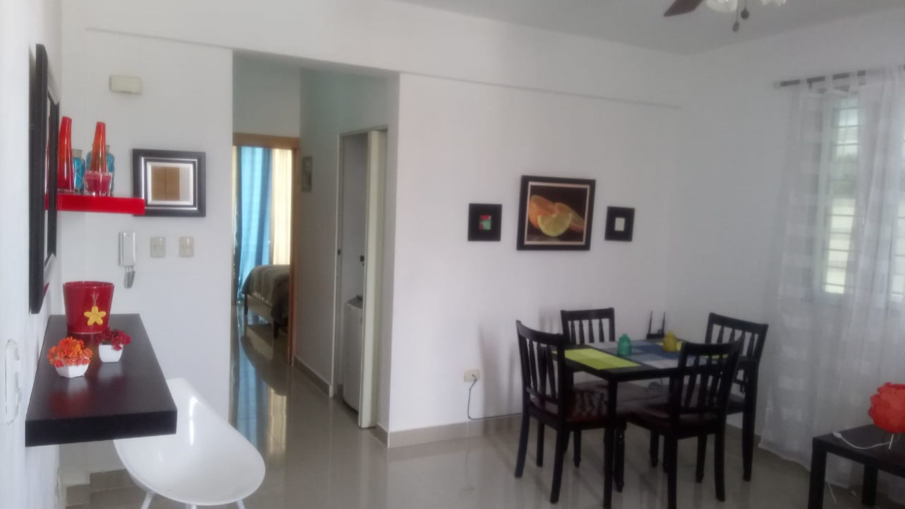 Un comedor con una mesa y sillas, una silla blanca, un cubo rojo y un cuadro en la pared.