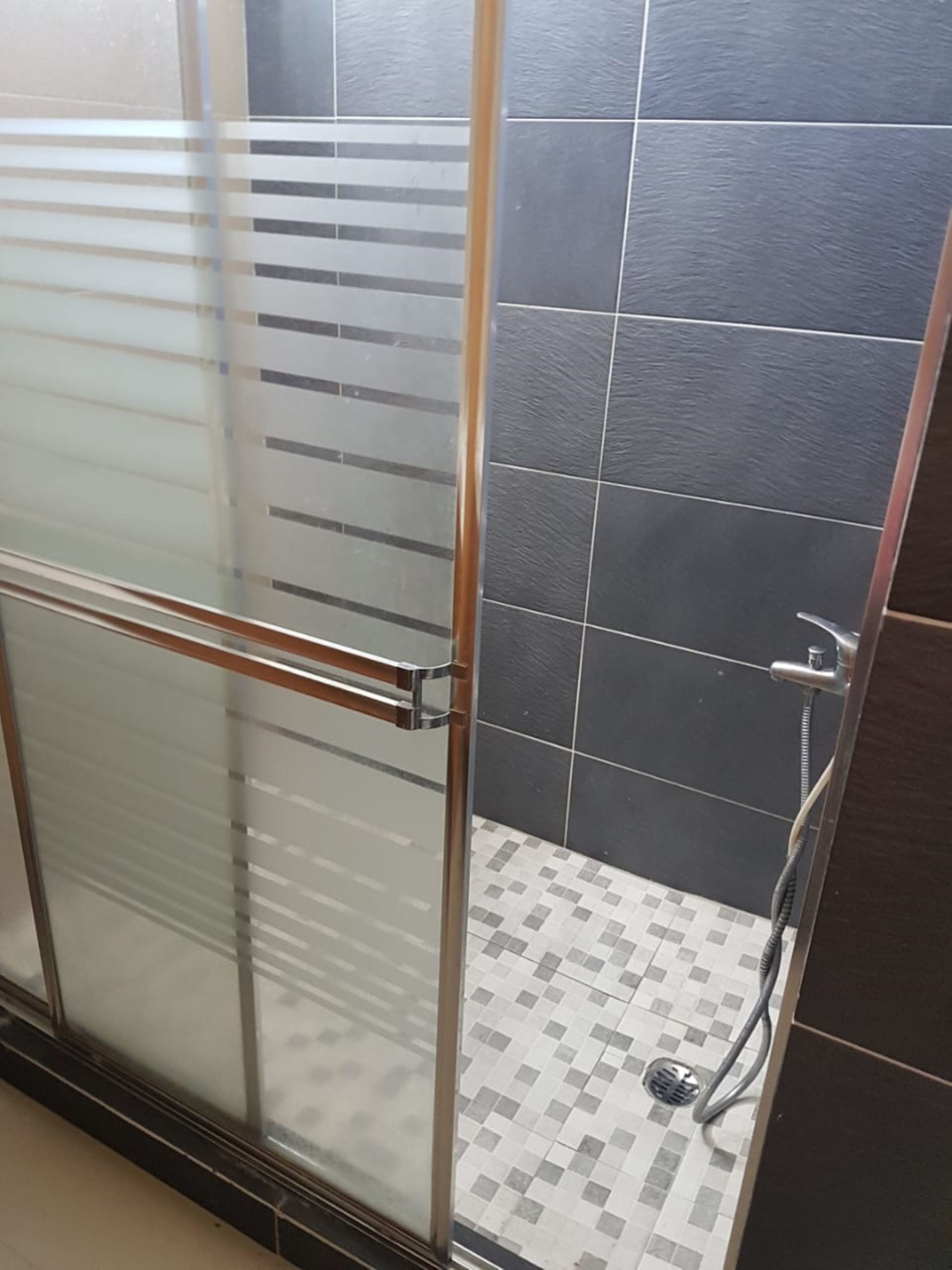 A shower area with a glass door, tiled walls, and a tiled floor.