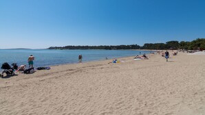 A wide sandy beach with clear blue water, a few people, and some beach equipment.