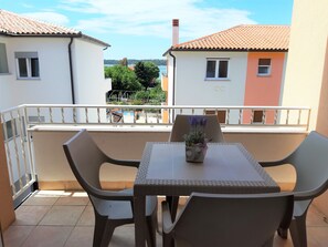 A balcony with a table and chairs, a flower vase, and a view of neighboring buildings and trees. - Apartment Medulin, 200 m from the sea, 600 m from the sandy beach (Medulin)