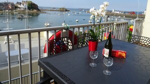 Een balkon met een tafel, twee wijnglazen, een champagnefles en een rode doos gebak.