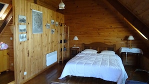 Een knus slaapkamer in een houten chalet, met een bed, twee nachtkastjes met lampen, een radiator, en een houten plank met foto's.