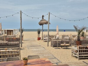 A beachside restaurant with outdoor seating, thatched umbrellas, and string lights.