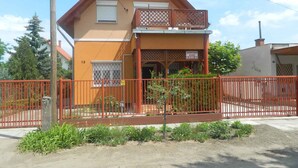 A two-story building with a balcony, a small garden area, and a red fence. - Holiday apartment in a nice area (Cserkeszőlő)