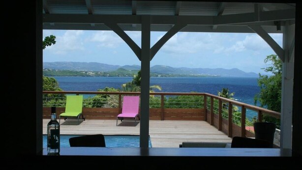 Un espacio al aire libre techado con piscina, dos sillas reclinables y vistas al mar y las montañas.