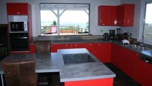 Una cocina moderna con armarios rojos, una isla central y vistas al océano.