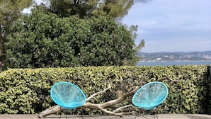 Una piscina amb dues cadires blaves sobre un pont de fusta, envoltada de vegetació i amb vista a un paisatge urbà llunyà.