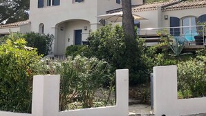 Edifici de dues plantes amb teulada de rajola, un balcó amb cadires i una zona de jardí amb diverses plantes.