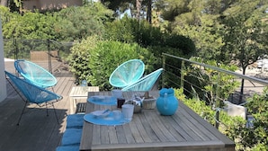 Una terrassa de fusta amb taula preparada per dinar, envoltada de coixins blaus i cadires de vimet.