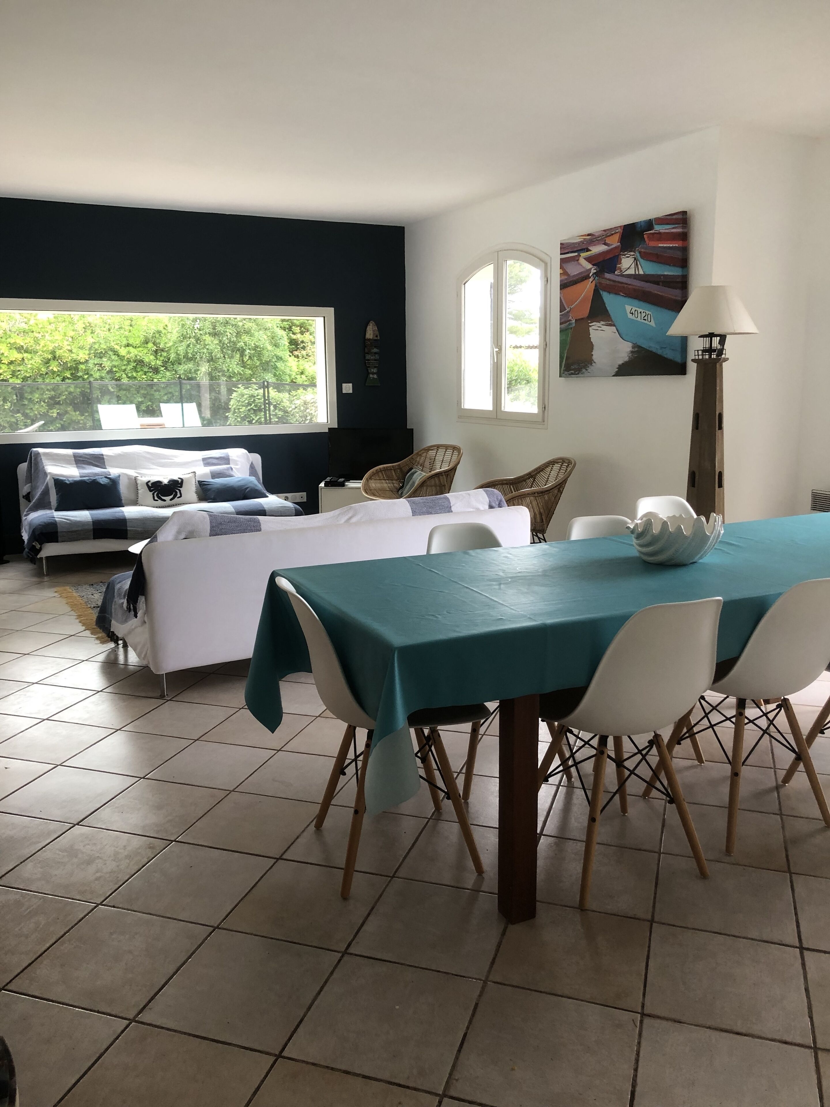 Ein Zimmer mit Esstisch, Stühlen, einer Couch und einem Fernseher. Es gibt Fenster mit Blick auf Grünflächen.