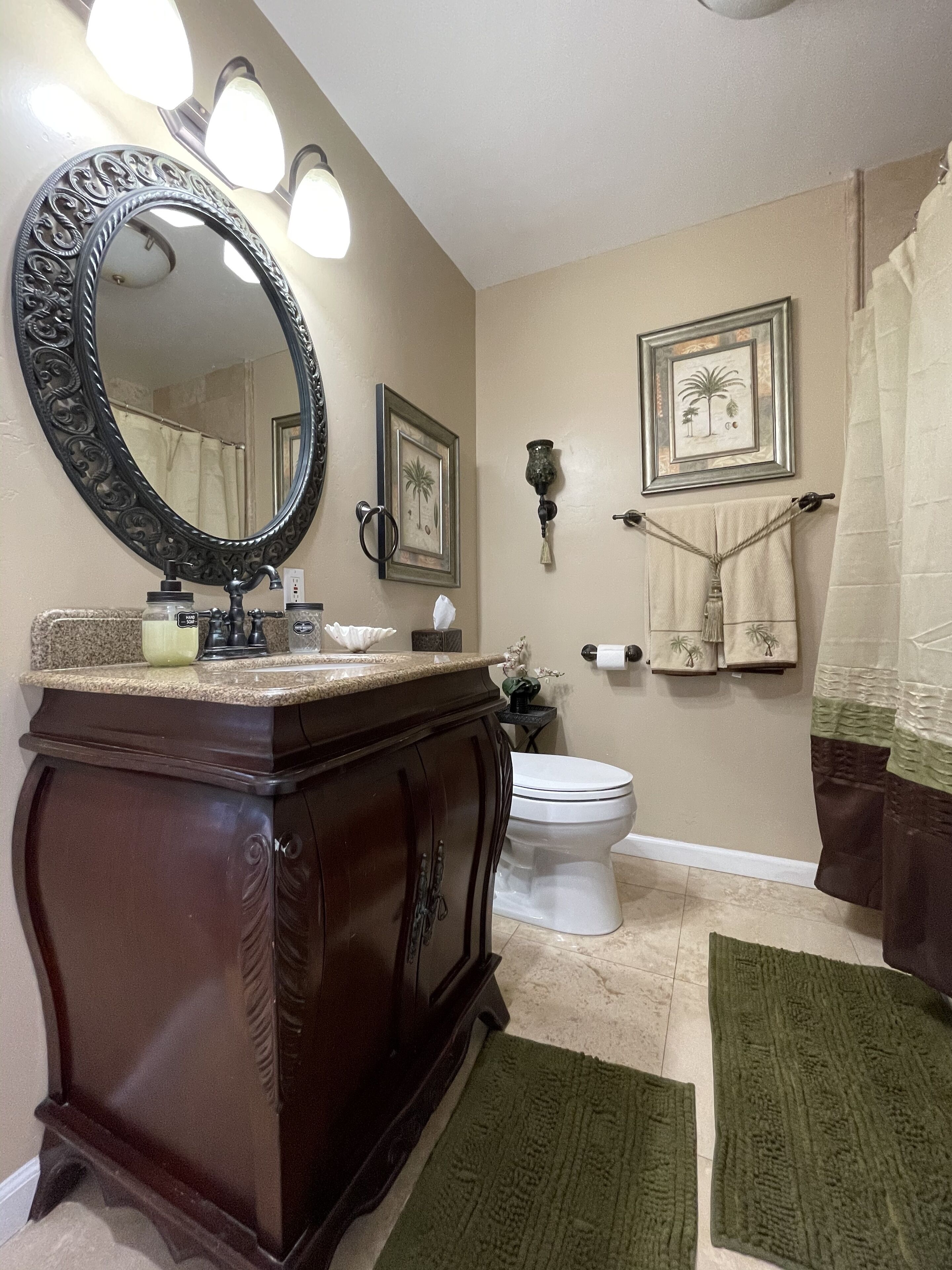 A bathroom with a vanity, sink, mirror, toilet, towel rack, and decorative wall art.
