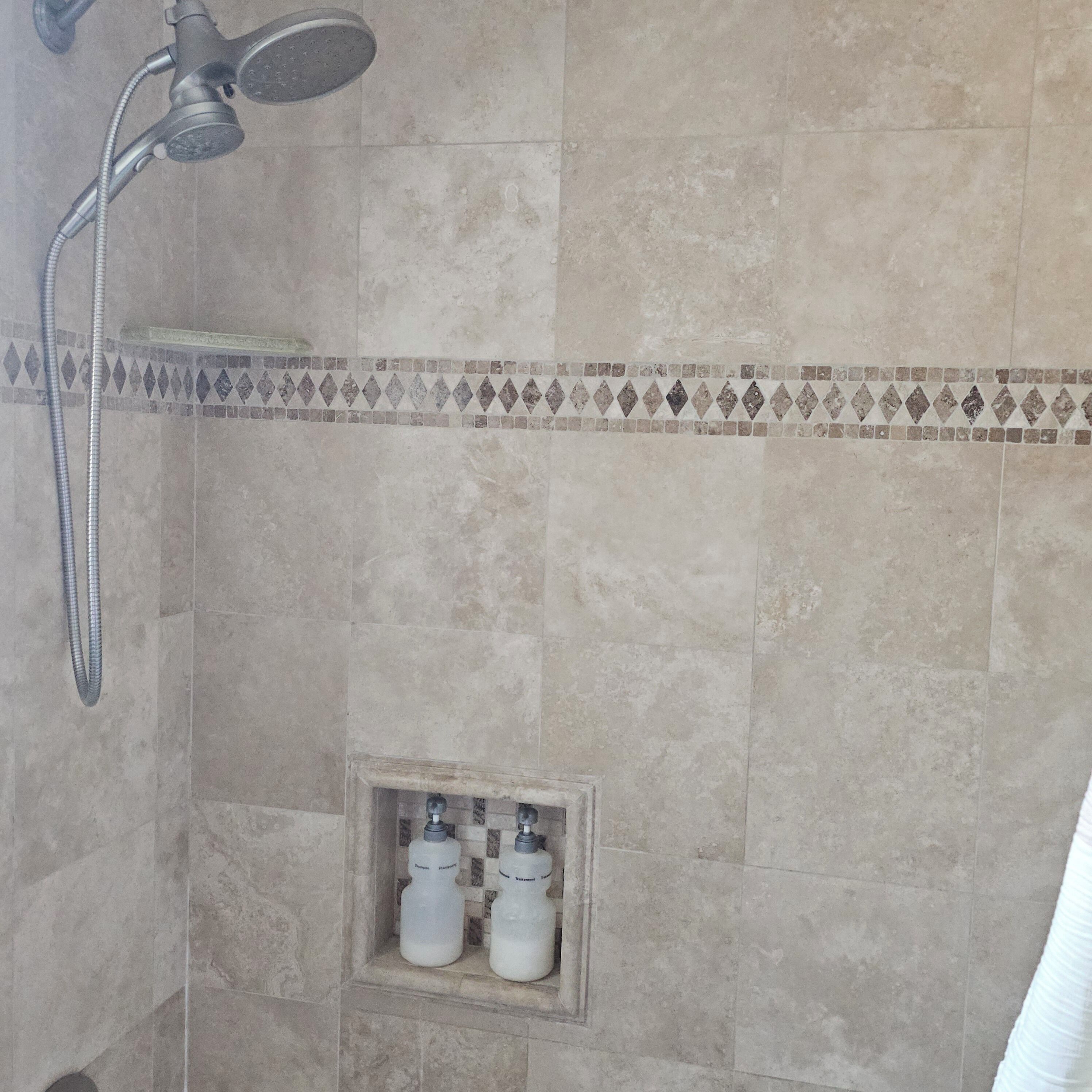 Un espace douche équipé d’un pommeau de douche à main, d’une étagère intégrée et de deux bouteilles de shampoing et d’après-shampoing.